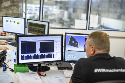 Mitarbeiter sitzt vor zwei Monitoren auf denen man CAD Konstruktionen sieht